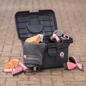 Open black pet grooming kit on a brick surface, containing pink-handled brushes, a sponge, and a gray Waldhausen towel with the logo on it.