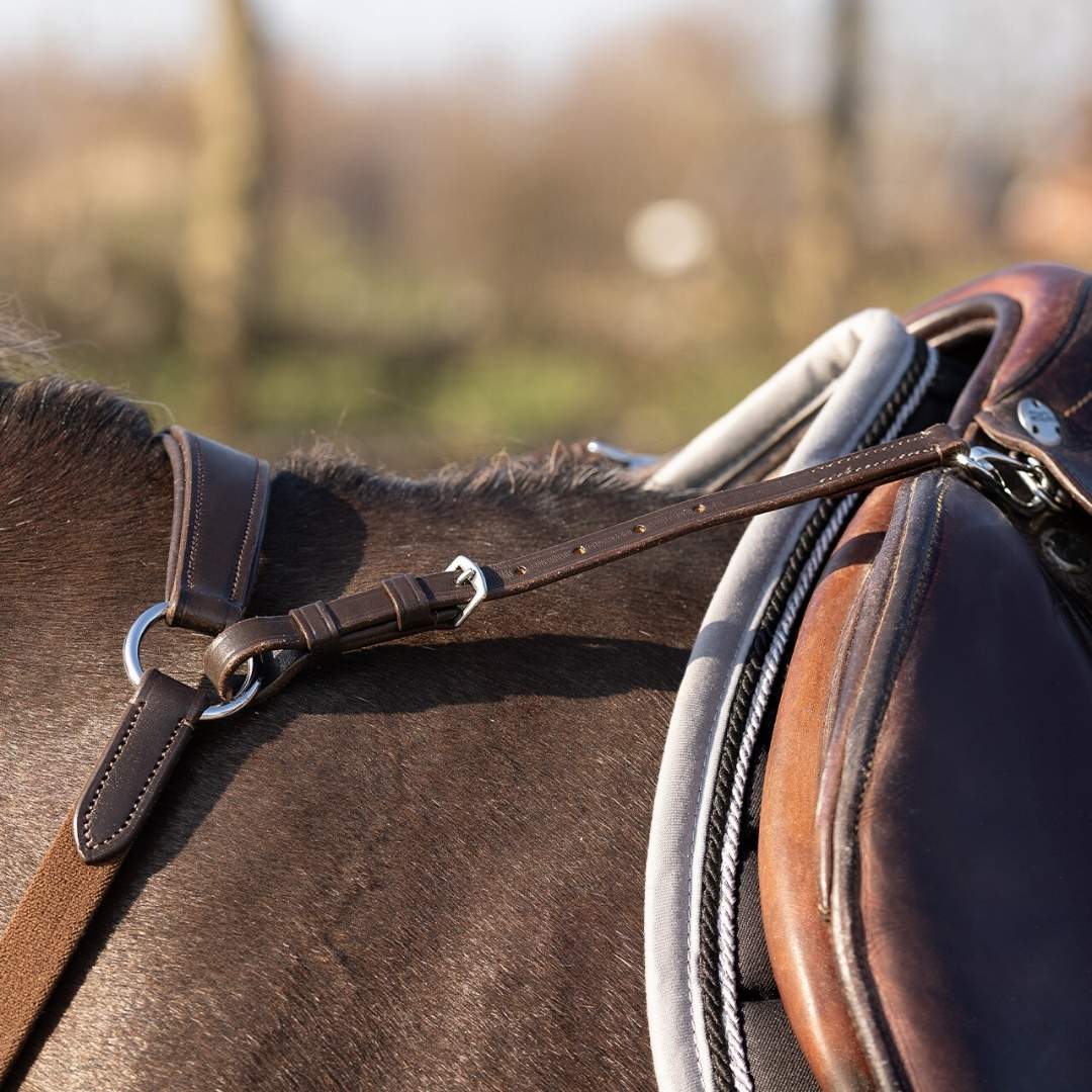 Close-up of a brown leather saddle strapped to a dark horse, outdoors.