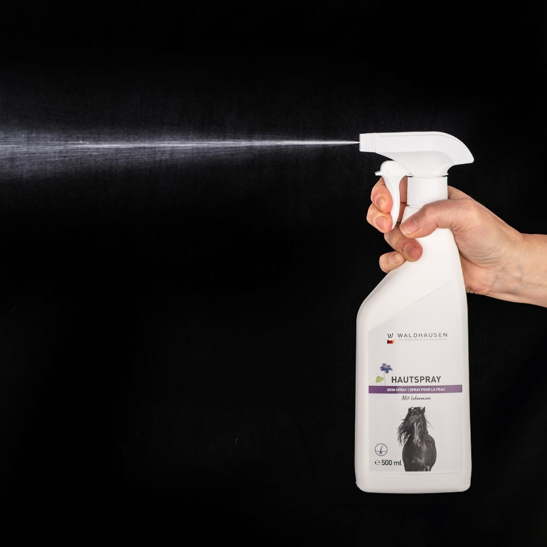 A hand pressing a white spray bottle, releasing a fine mist against a black background (dog care product).