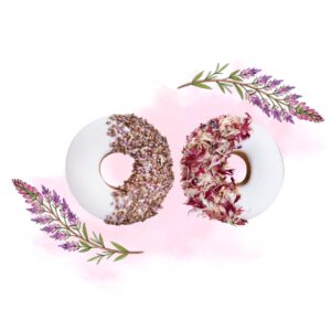 Two white-glazed donuts with floral toppings—one coated in crushed seeds, the other with dried petals—on a pale pink watercolor background with lavender sprigs.