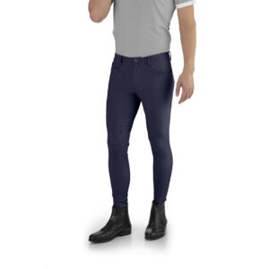 Full-length view of a person wearing navy riding tights, a light gray shirt, and black ankle boots, standing against a white background.