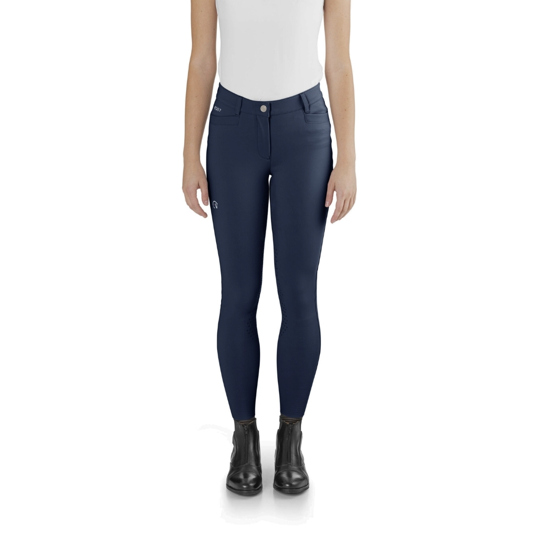 Front view of a person wearing navy riding breeches with a white top and black boots (model pose).