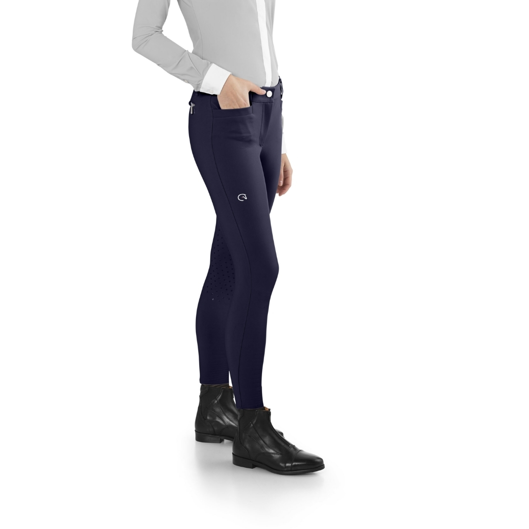 Navy women's riding breeches with a small logo, front pockets, and subtle perforated panels, paired with black ankle boots.