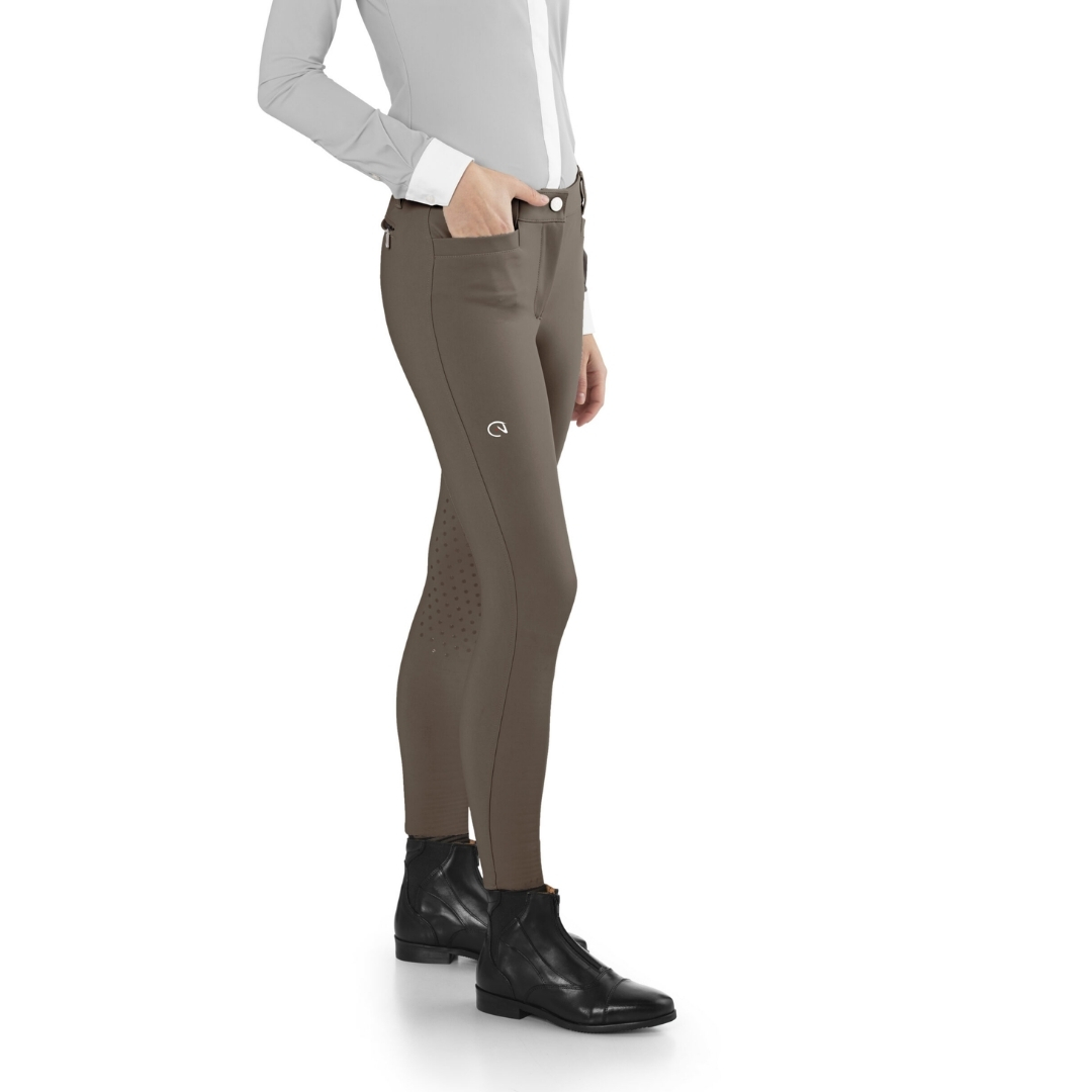 Side view of a person wearing taupe riding breeches with silicone grip dots on the inner calf, paired with black ankle boots.