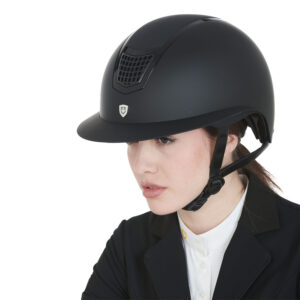 Woman in a matte black riding helmet and formal riding jacket, looking slightly to the left.
