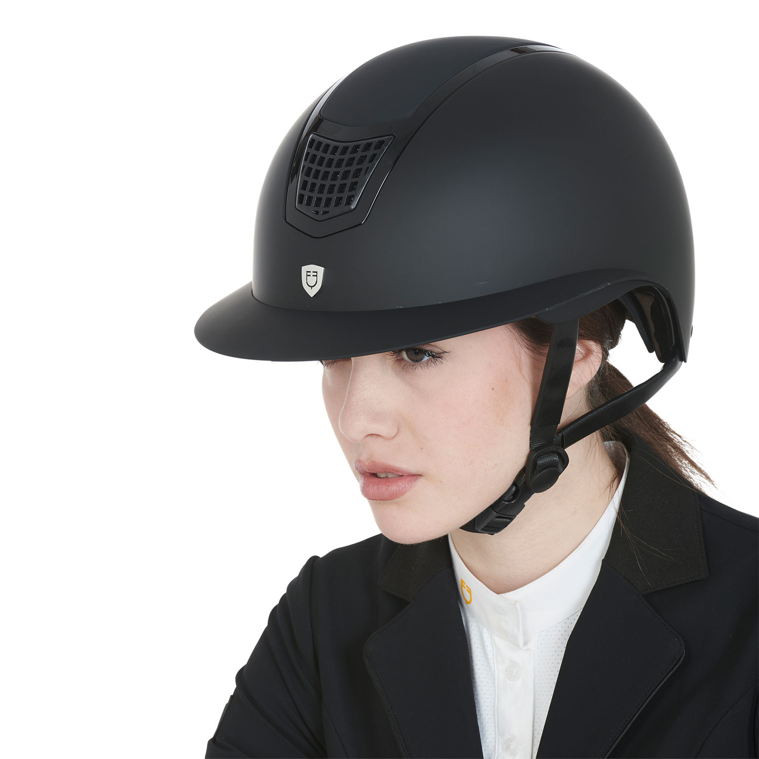 Woman in a matte black riding helmet and formal riding jacket, looking slightly to the left.