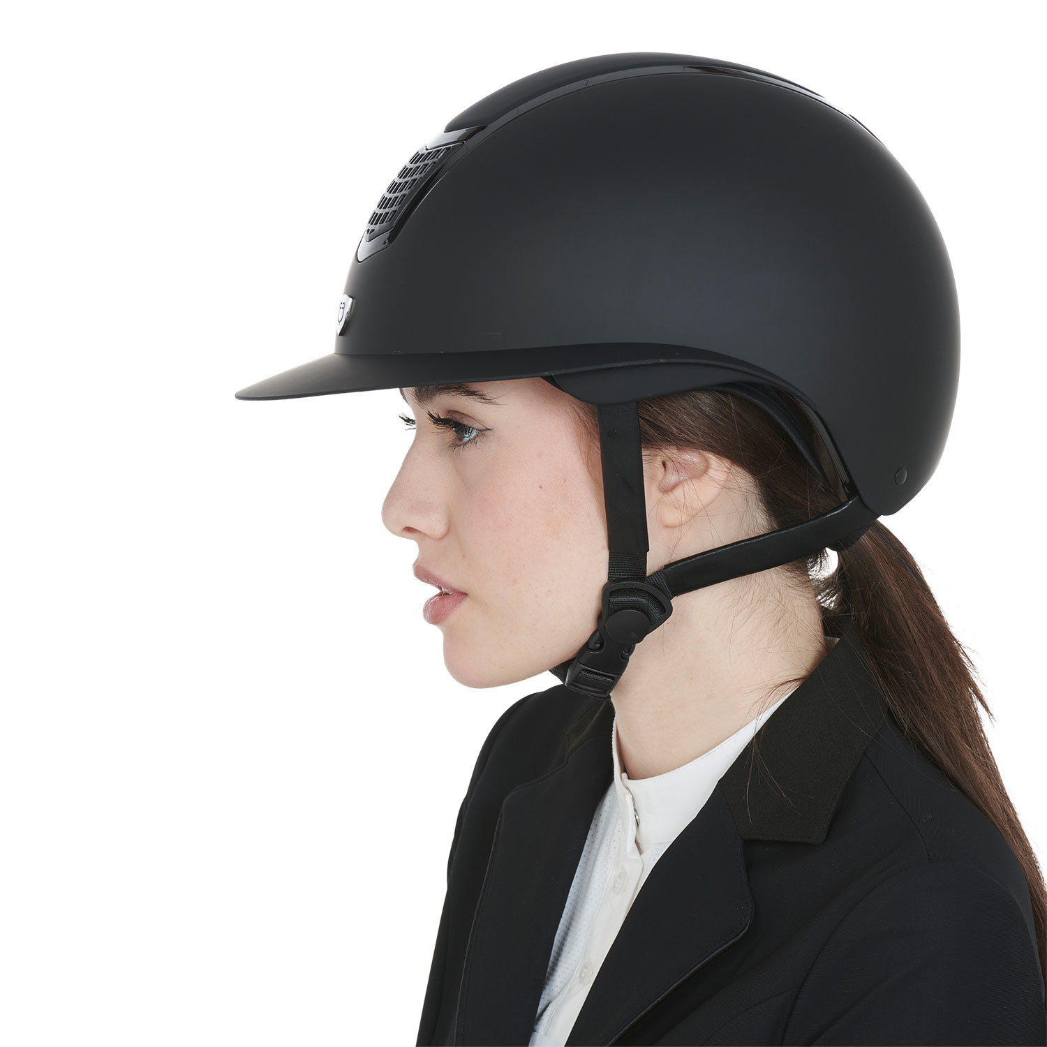 Profile view of a person wearing a matte black equestrian helmet with a chin strap, looking left.