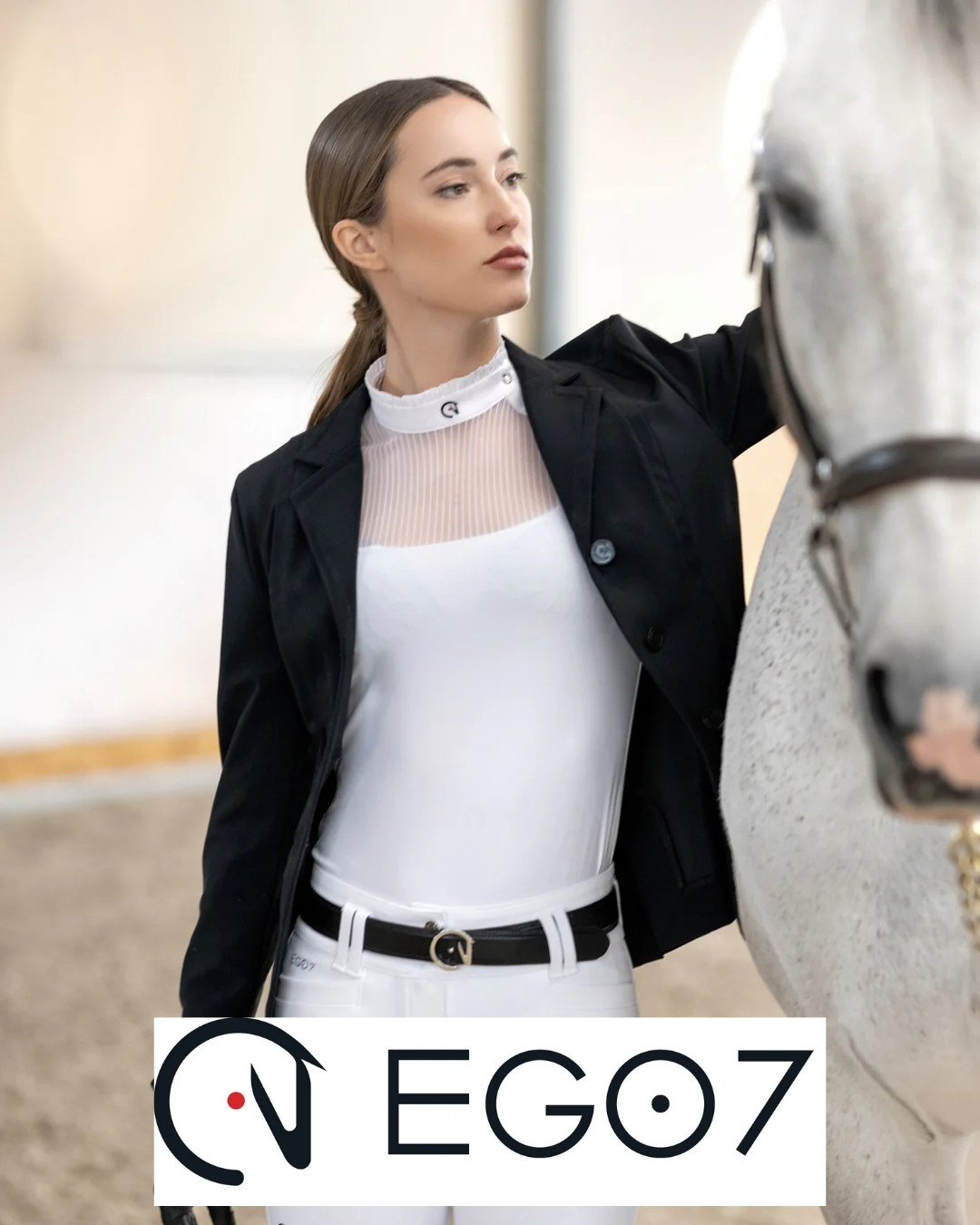Woman in white riding top and black blazer stands beside a gray horse, logo “EGO7” at bottom.