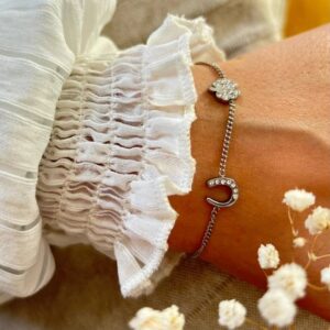 Silver bracelet with a bejeweled crescent moon charm on a wrist beside a white ruffled sleeve.