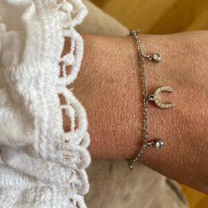Wrist wearing two silver bracelets: a chain bracelet with a crystal-encrusted crescent moon charm and a small round crystal charm against a white lace sleeve.